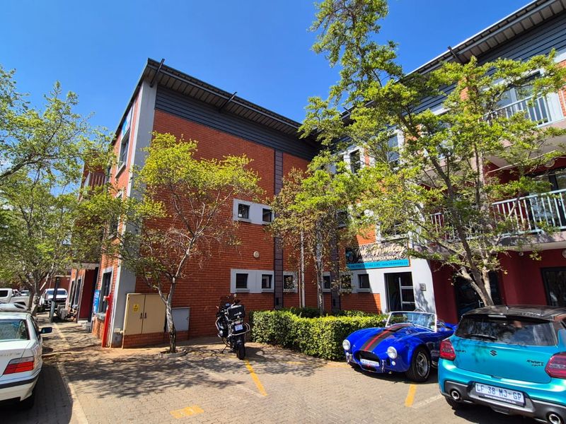 Front elevation of a multi-story industrial or commercial building featuring red brick construction, metal roofing, and dedicated paved parking spaces.