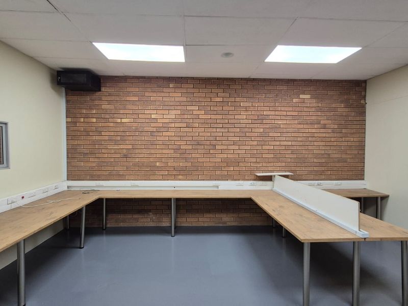 A functional office space featuring a brick accent wall, built-in desk workstations, recessed lighting, and durable vinyl flooring.