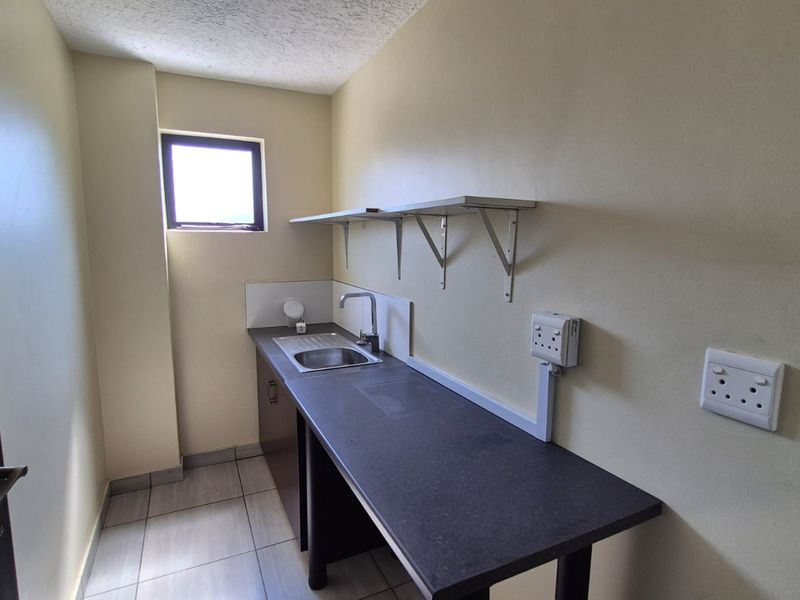 A functional scullery or utility area featuring a stainless steel sink, laminate countertop, and wall-mounted shelving with tiled flooring.