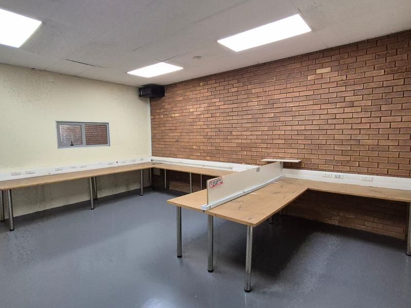 A functional office space featuring built-in desk workstations, exposed brick feature wall, and recessed ceiling lighting, suitable for a professional industrial workspace.