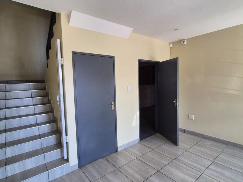 A clean, functional hallway featuring tiled flooring, a staircase with a metal handrail, and access to adjacent rooms through internal doors.