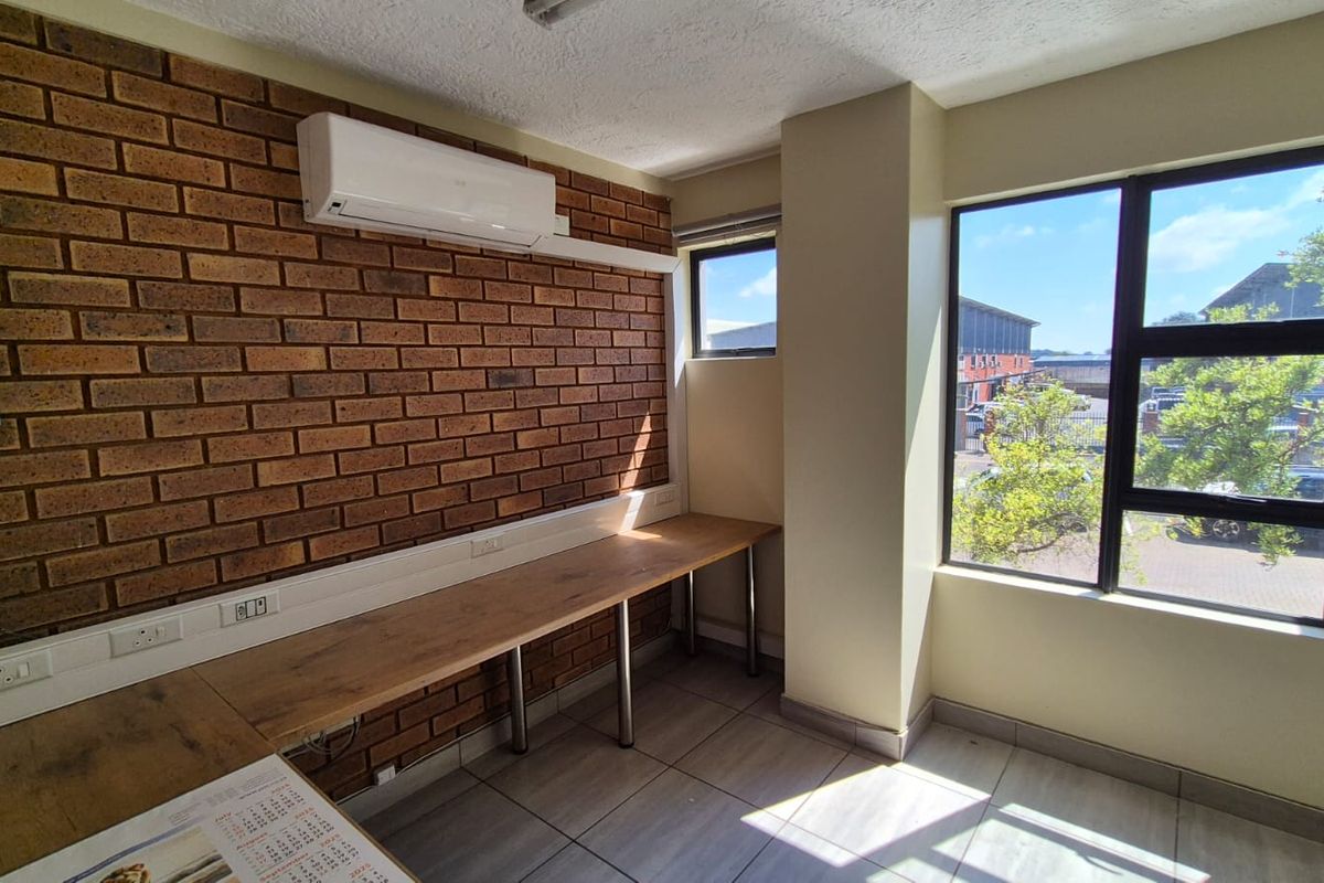 A bright, functional office space featuring an exposed brick feature wall, built-in desk, split-system air conditioning, and large windows providing natural light.