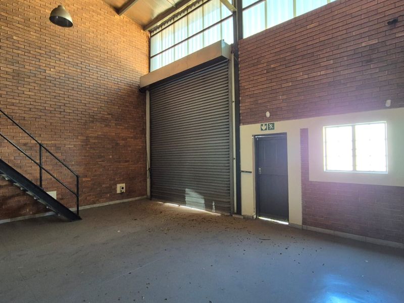 Spacious industrial utility area featuring exposed brick walls, a large roller shutter door, and a metal staircase leading to an upper level.