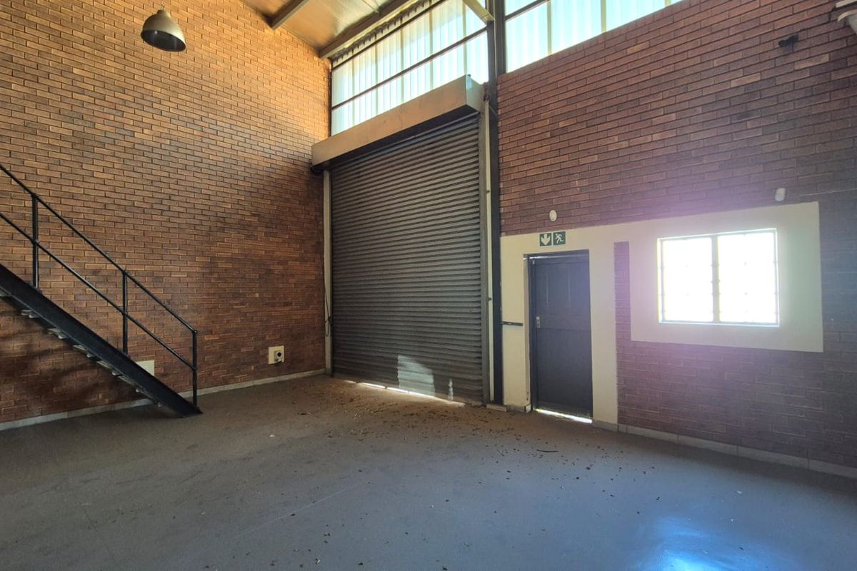 Spacious industrial utility area featuring exposed brick walls, a large roller shutter door, and a metal staircase leading to an upper level.