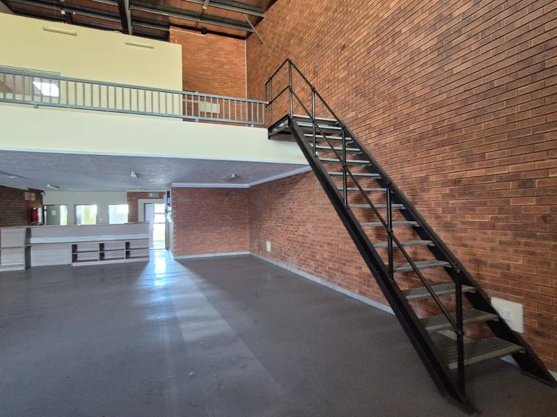 Spacious industrial unit featuring exposed brick walls, a mezzanine level with metal staircase, and an open-plan layout suitable for various commercial or storage uses.