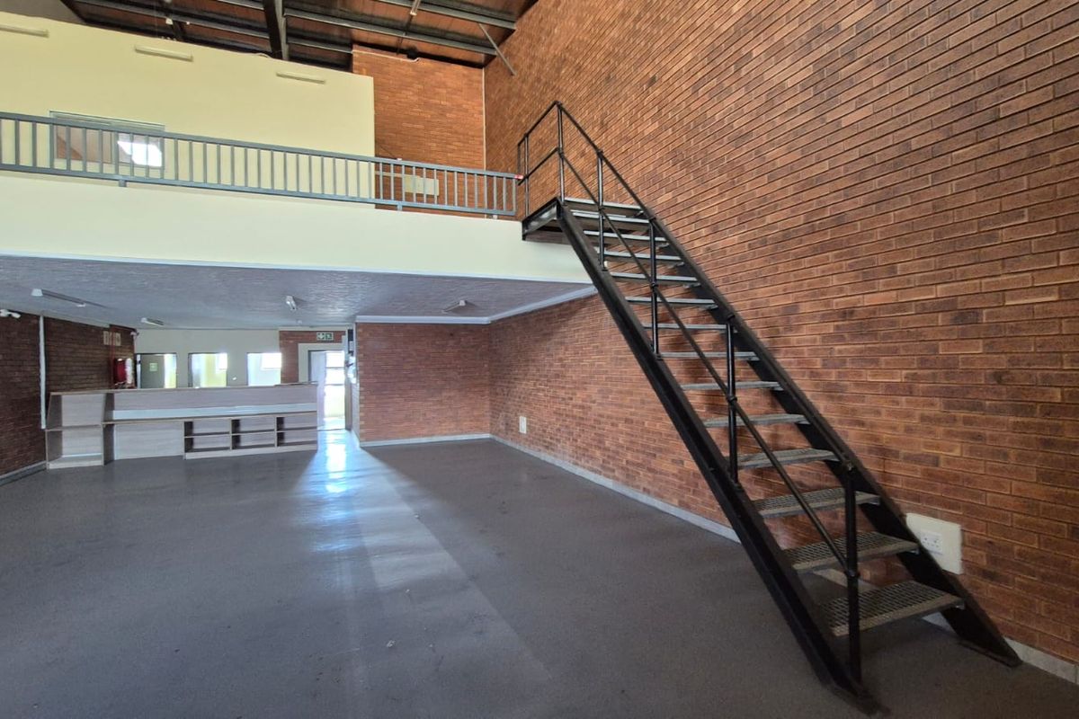 Spacious industrial unit featuring exposed brick walls, a mezzanine level with metal staircase, and an open-plan layout suitable for various commercial or storage uses.