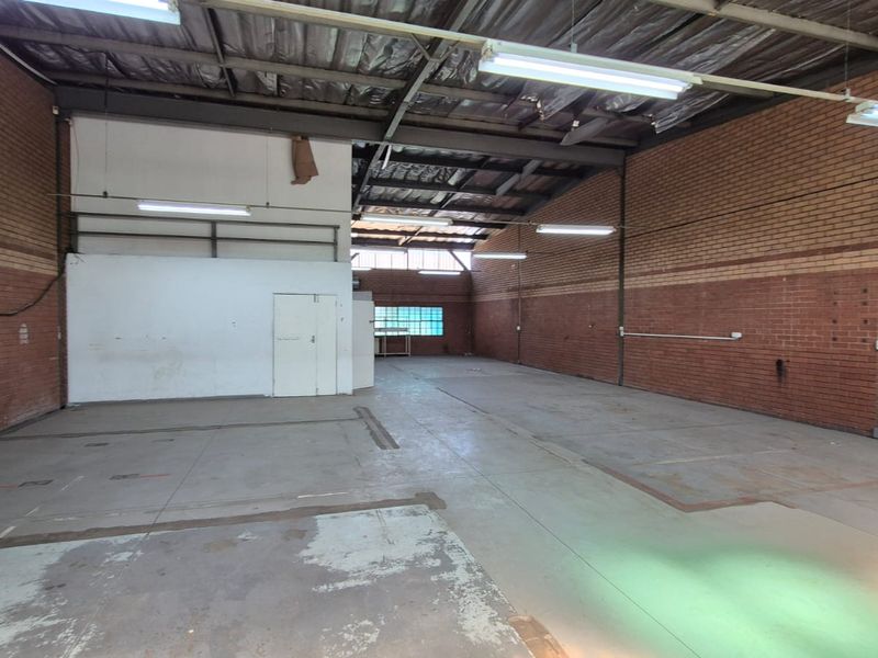 Spacious industrial warehouse unit featuring exposed brick walls, concrete flooring, and high-clearance metal roofing with integrated fluorescent lighting.