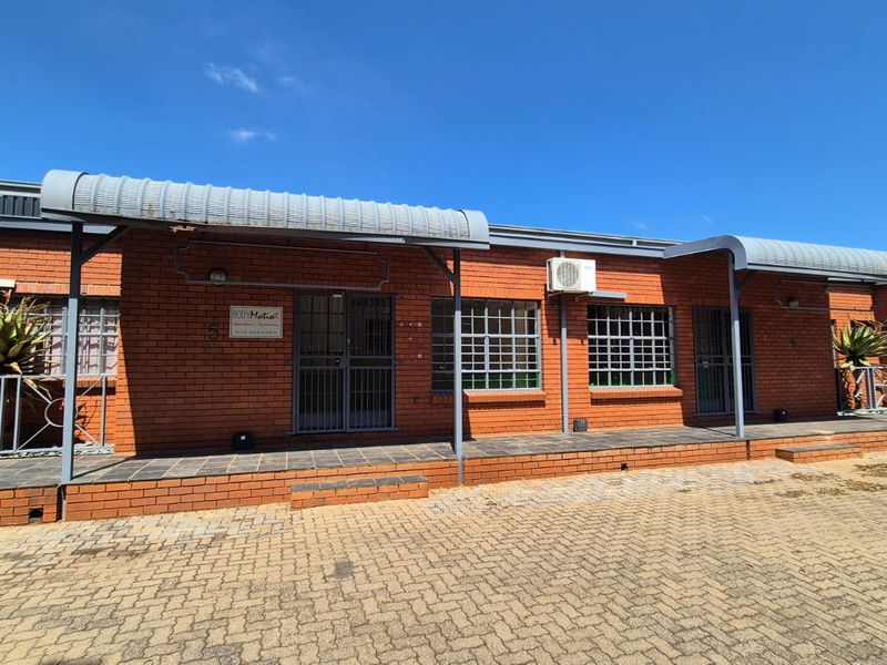 Front elevation of an industrial brick building featuring metal awnings, security gates, and paved access area with external air conditioning units.