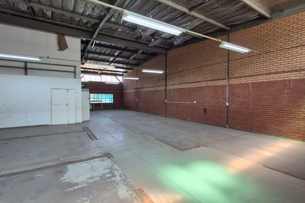 Spacious industrial warehouse unit featuring exposed brick walls, concrete flooring, high ceilings with steel trusses, and functional fluorescent lighting throughout.