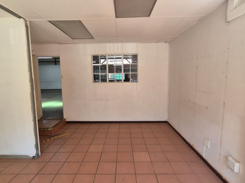 A vacant office space featuring tiled flooring, a suspended ceiling, and an internal window looking into the warehouse area.