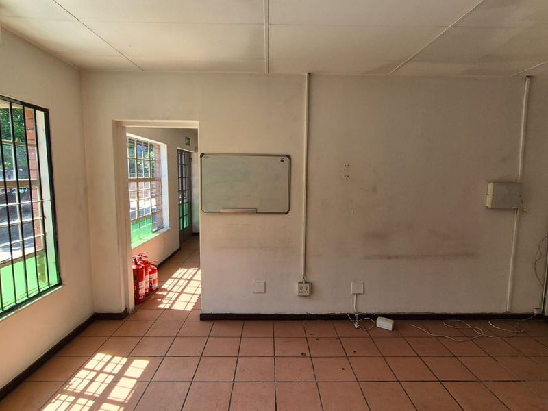 An empty office space featuring tiled flooring, security bars on windows, wall-mounted whiteboard, and air conditioning unit, requiring minor cosmetic repairs.