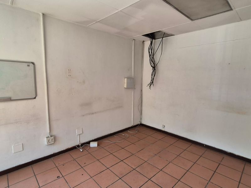 An empty office space featuring tiled flooring, a suspended ceiling, and exposed electrical wiring, requiring maintenance and cosmetic updates.