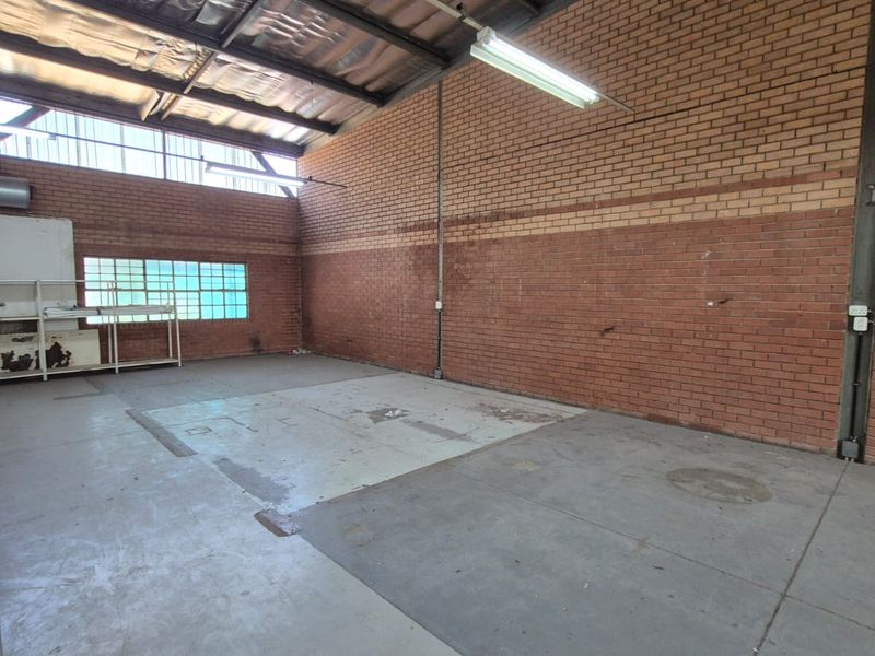 An open-plan industrial utility space featuring exposed brick walls, concrete flooring, and high-clearance metal roofing with integrated fluorescent lighting.