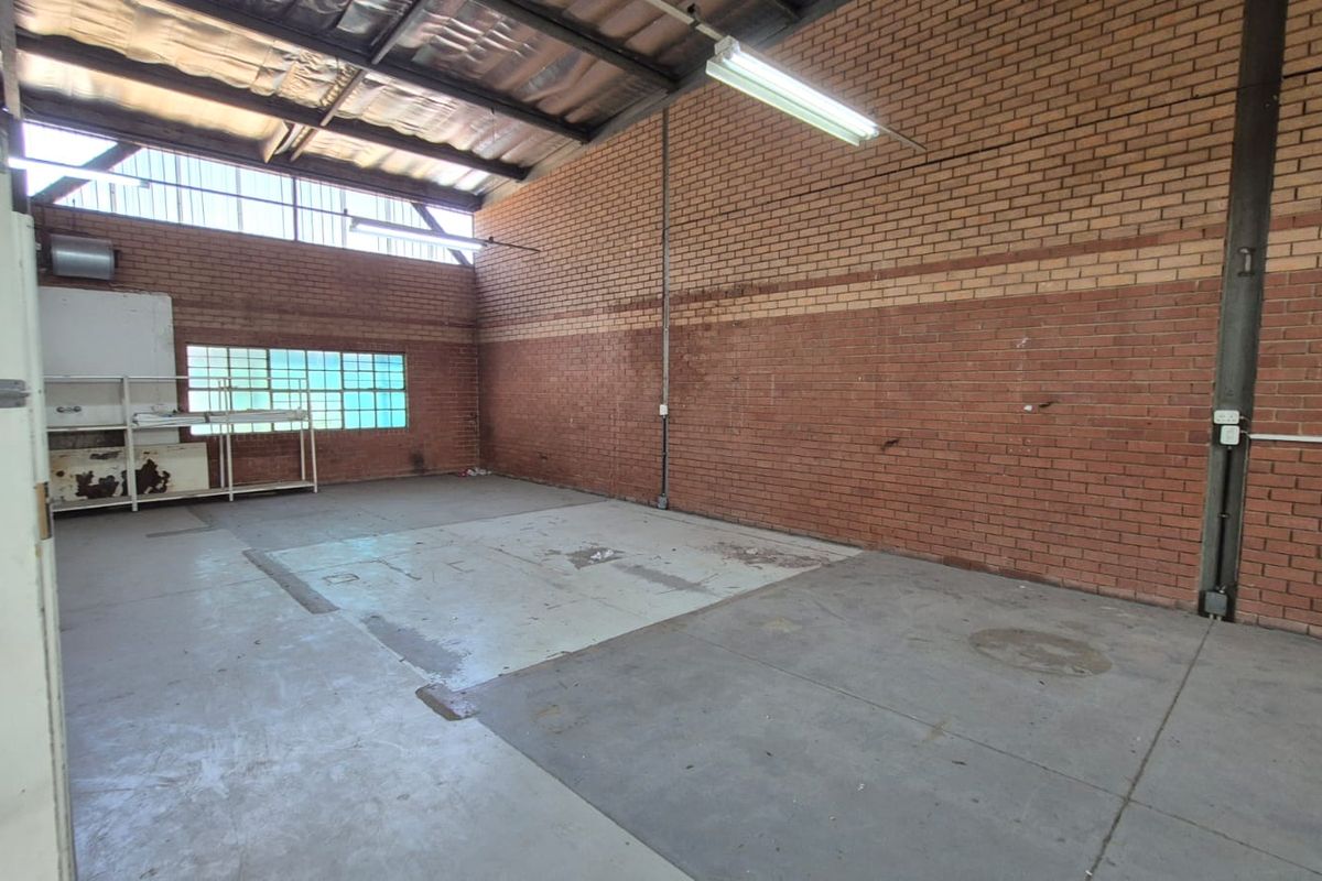 An open-plan industrial utility space featuring exposed brick walls, concrete flooring, and high-clearance metal roofing with integrated fluorescent lighting.