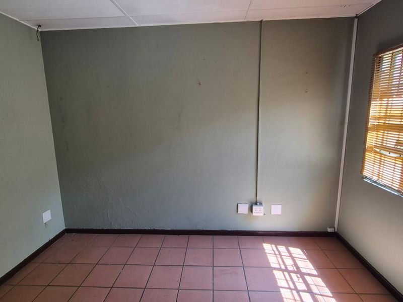 An empty office space featuring tiled flooring, surface-mounted electrical conduits, and a suspended ceiling, suitable for a functional workspace.