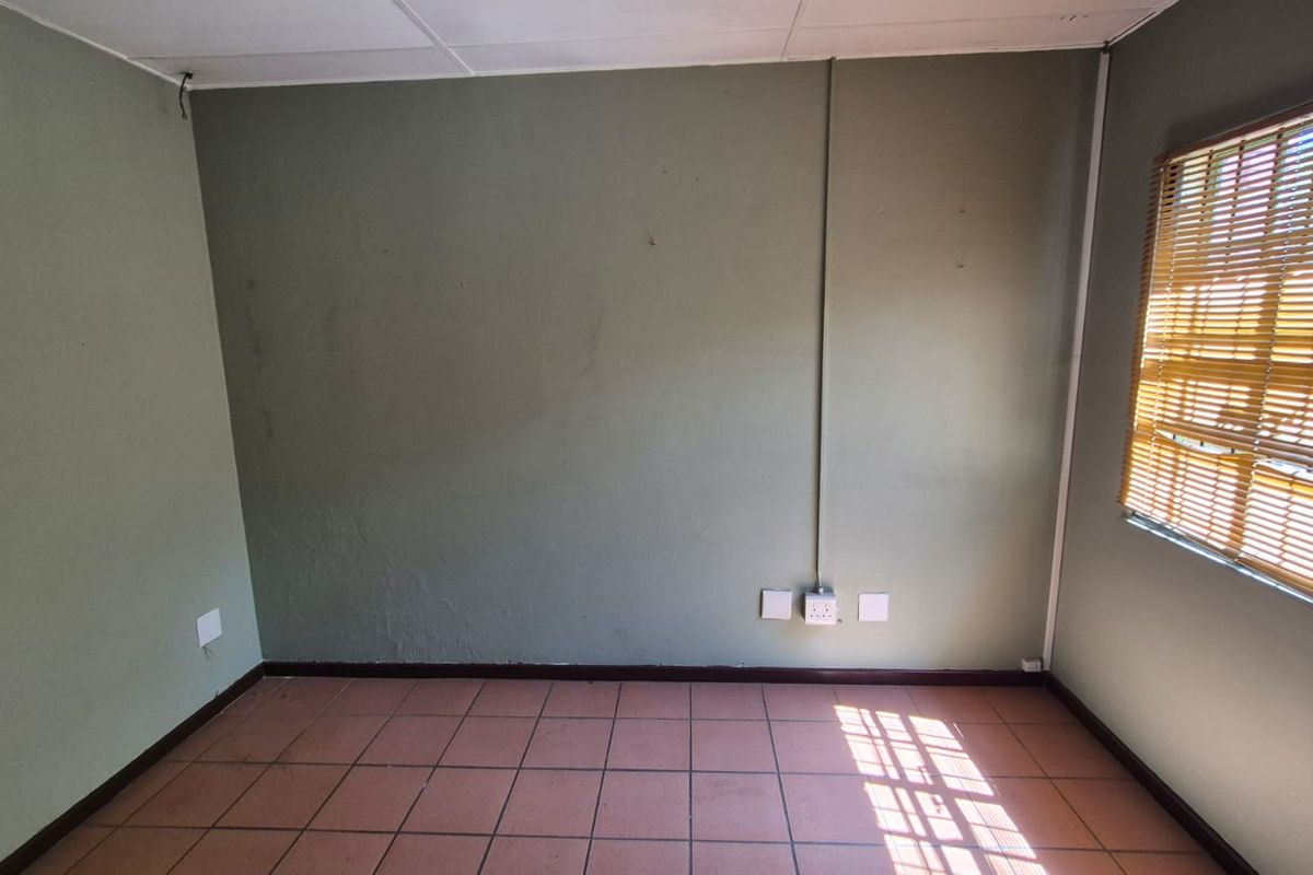 An empty office space featuring tiled flooring, surface-mounted electrical conduits, and a suspended ceiling, suitable for a functional workspace.