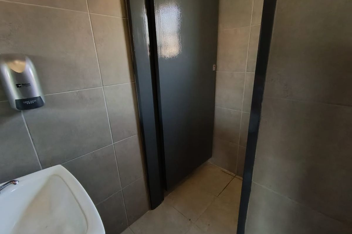 A functional office restroom featuring tiled walls and flooring, a wall-mounted basin, and a private stall door.