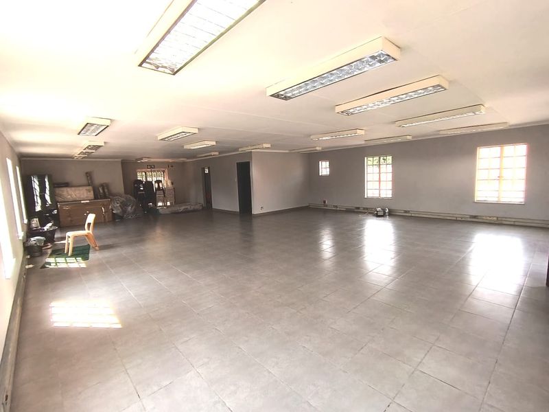 A spacious, open-plan office area featuring tiled flooring, recessed fluorescent lighting, and large windows providing ample natural light.