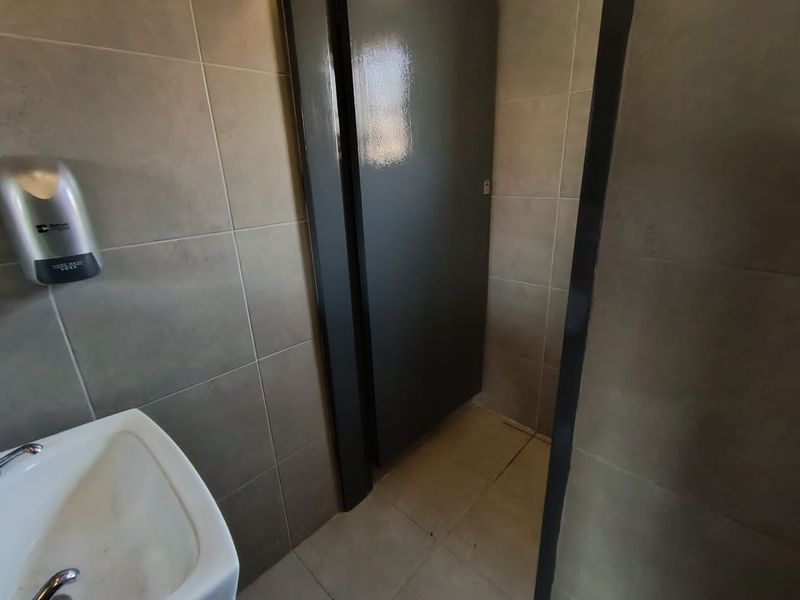 A functional office restroom featuring tiled walls and flooring, a wall-mounted basin, and a private stall door.