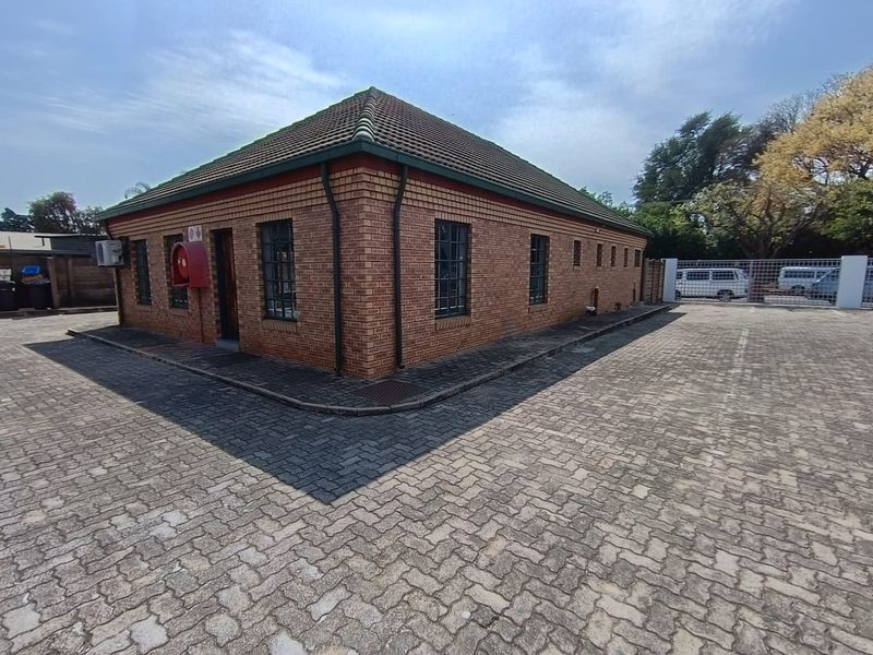 Exterior view of a single-story face-brick office building featuring a tiled roof, paved parking area, and external fire safety equipment.