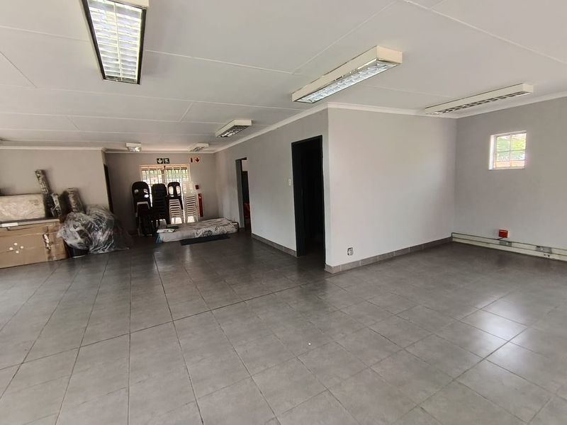 Spacious open-plan office area featuring tiled flooring, recessed fluorescent lighting, and neutral wall finishes, suitable for a flexible workspace layout.