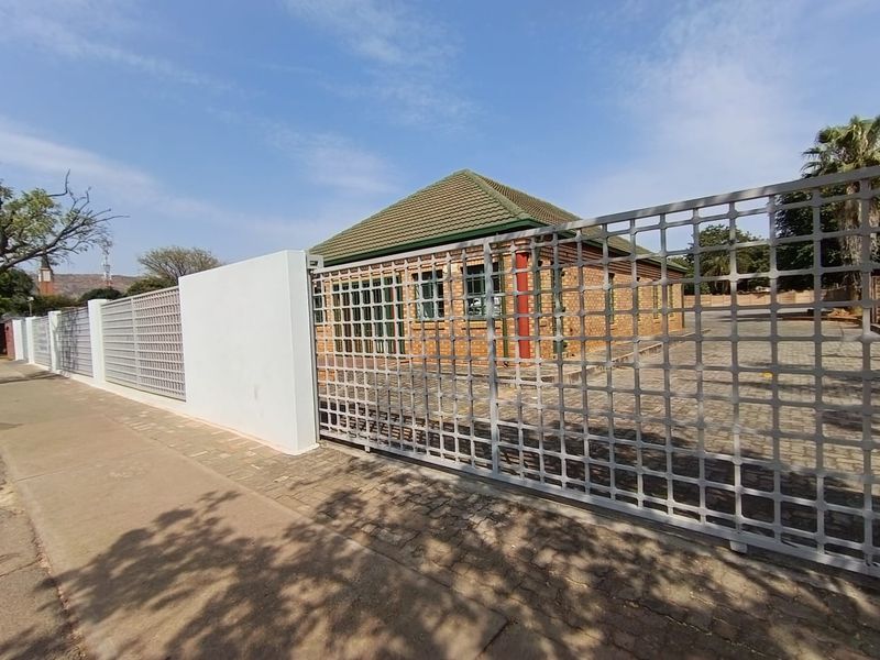 A secure office property featuring a face-brick exterior, tiled roof, and a large metal perimeter gate with paved driveway access.