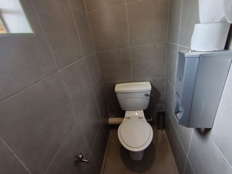 A compact office restroom featuring modern grey wall tiling, a standard white toilet, and a wall-mounted paper dispenser.