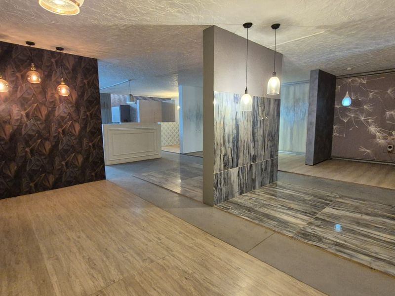 A spacious open-plan industrial showroom area featuring diverse flooring finishes, decorative wall panels, and modern pendant lighting throughout the interior space.