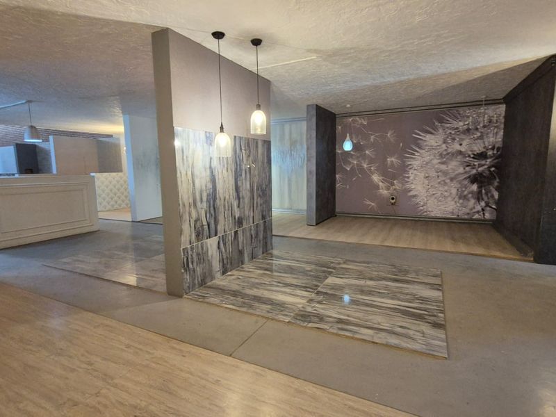 Spacious open-plan industrial showroom area featuring modern pendant lighting, decorative tiled feature walls, and a mix of laminate and tiled flooring.
