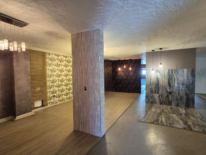 Spacious open-plan industrial area featuring decorative wall finishes, tiled feature columns, timber-look flooring, and modern pendant lighting throughout the versatile interior space.