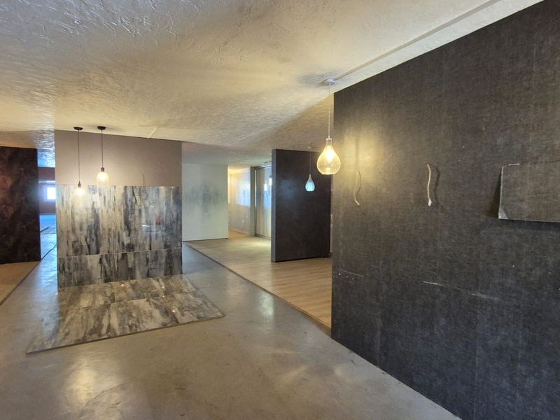 An open-plan industrial space featuring varied wall textures, pendant lighting, and a mix of concrete and laminate flooring, suitable for showroom or office use.