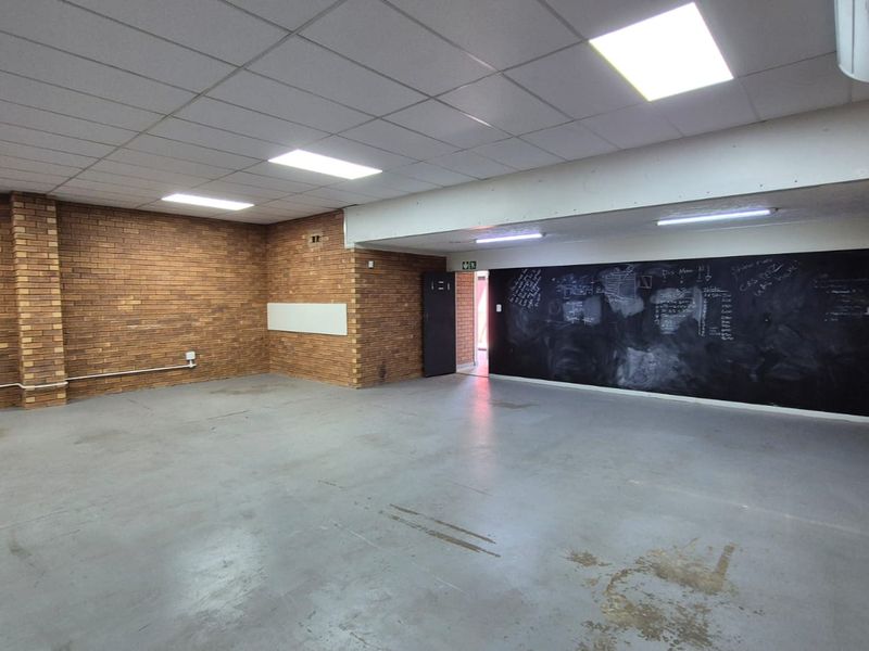 Spacious industrial office area featuring exposed brick walls, durable concrete flooring, suspended ceiling with recessed lighting, and a large integrated chalkboard wall.