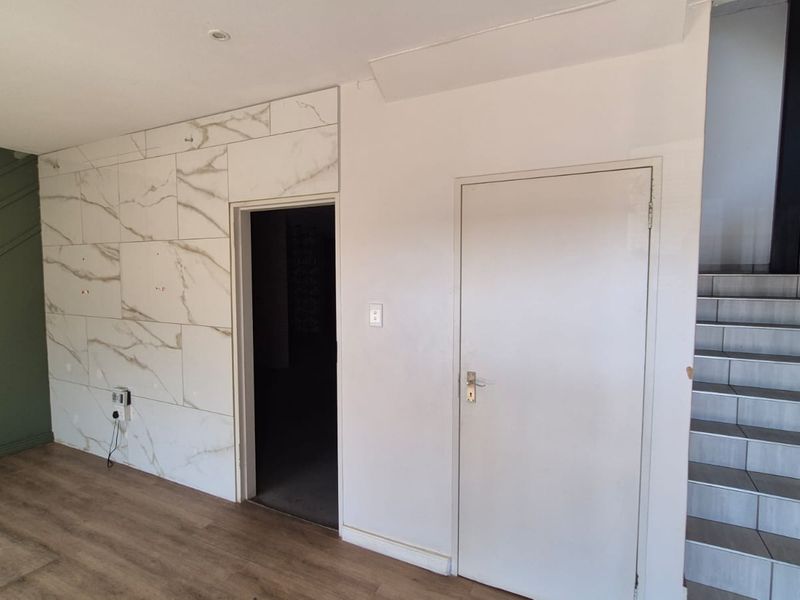 A bright hallway featuring marble-effect wall cladding, laminate flooring, and a tiled staircase with a handrail, presenting a clean and modern industrial aesthetic.