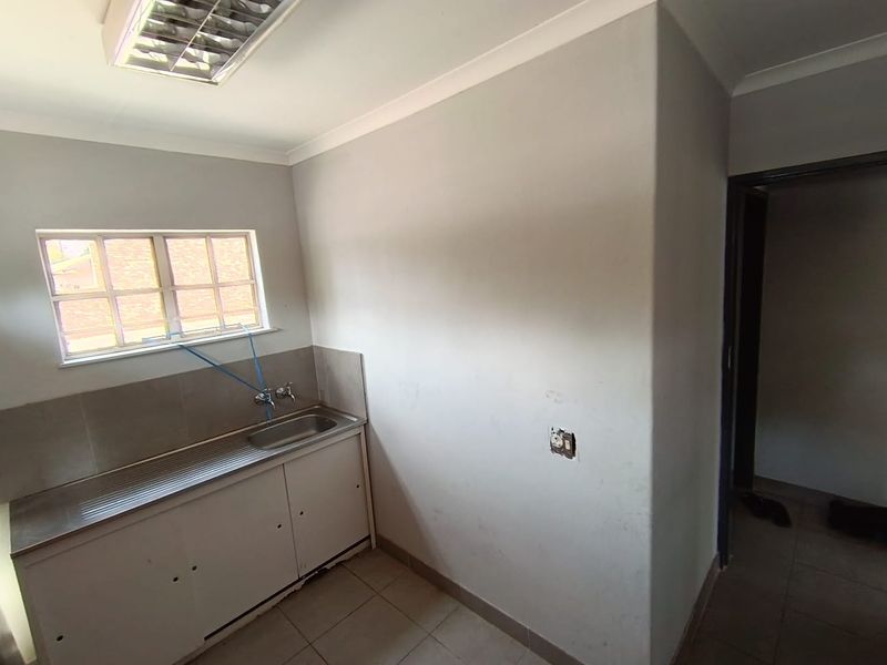 A functional utility space or scullery featuring a stainless steel sink, tiled splashback, and tiled flooring, suitable for office support or kitchen prep.