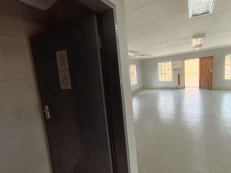 Spacious open-plan office area featuring tiled flooring, recessed fluorescent lighting, and a dedicated accessible restroom entrance.