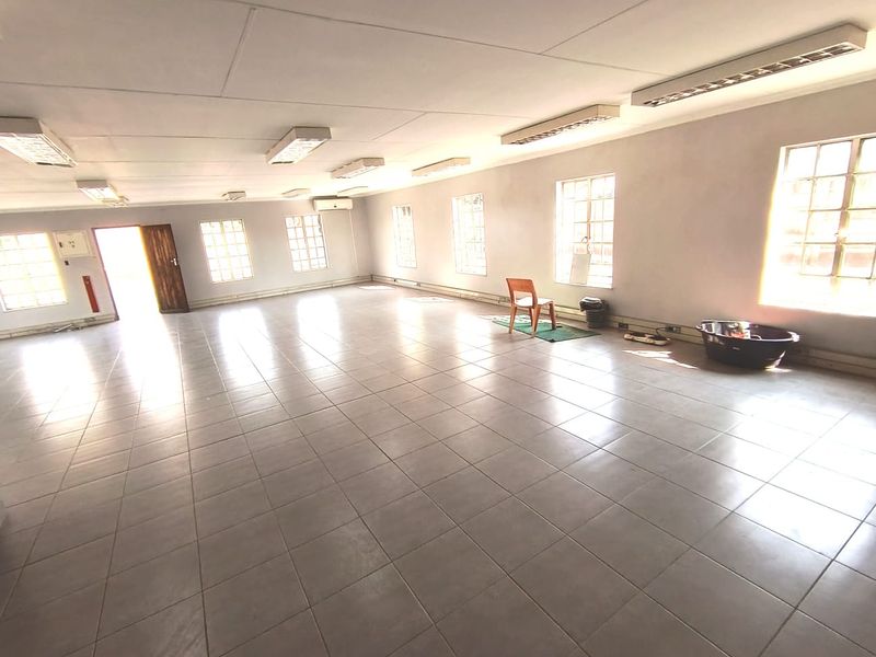 A spacious, open-plan office area featuring tiled flooring, multiple windows for natural light, and integrated fluorescent lighting fixtures.