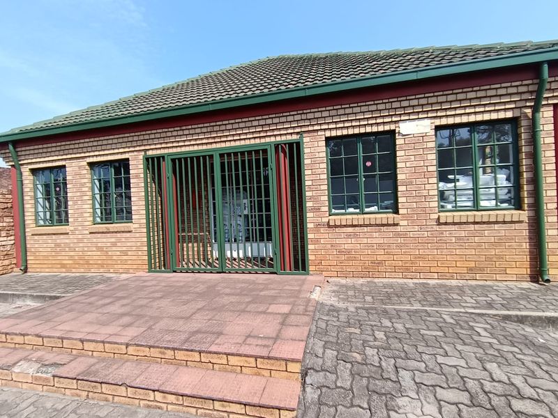 Front exterior view of a brick office building featuring a tiled roof, green-framed windows, and a secure metal entrance gate with paved access steps.
