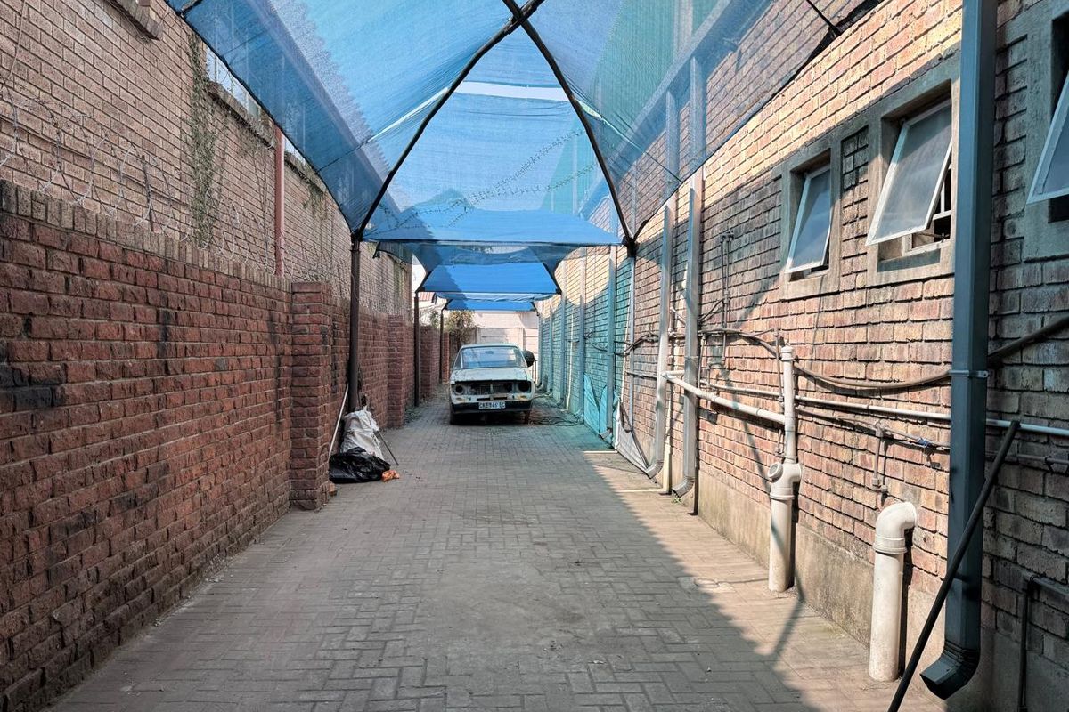 A narrow exterior service alley featuring paved flooring, exposed brick walls, and a blue shade cloth canopy structure.