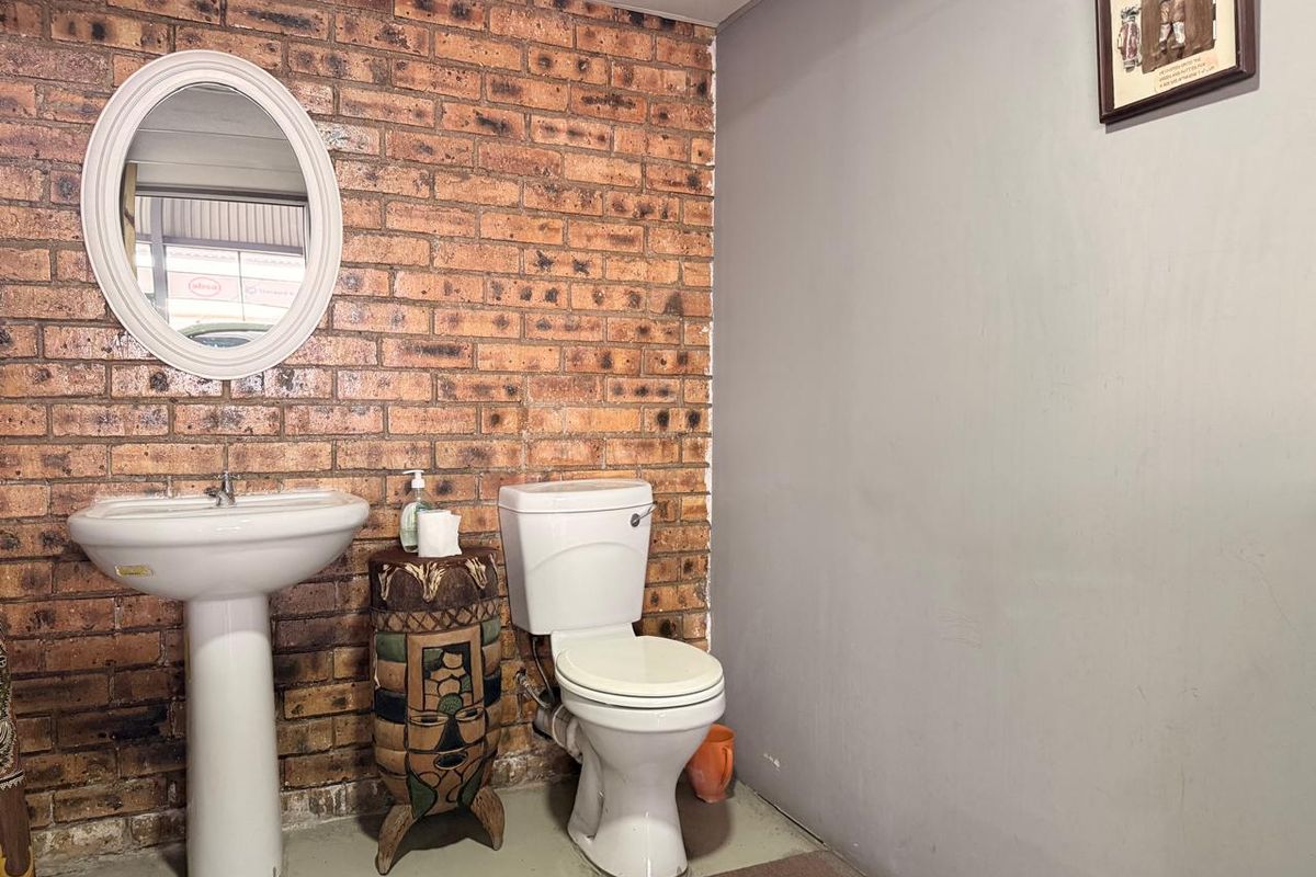 A functional bathroom featuring a pedestal basin and toilet against a rustic exposed brick feature wall.