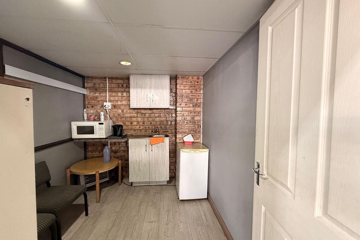 A compact kitchenette area featuring built-in cabinetry, a sink, and exposed brick wall detailing, suitable for a small office or utility space.
