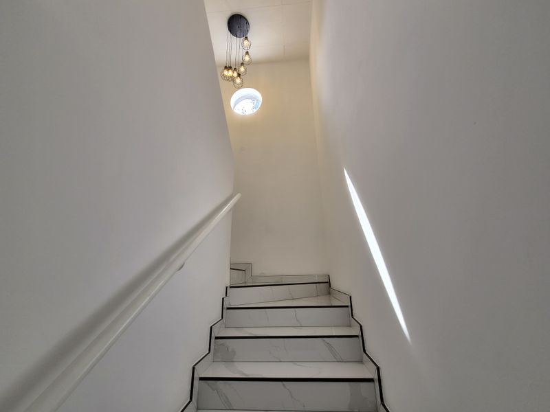 A clean, modern staircase featuring marble-look tiled steps, a sleek handrail, and a contemporary pendant light fixture.
