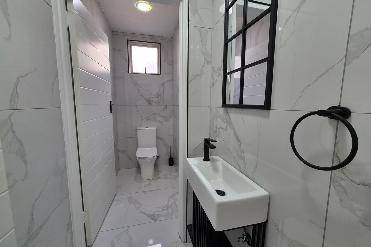 Modern guest bathroom featuring marble-look porcelain tiling, a sleek wall-mounted basin with black fixtures, and a contemporary black-framed mirror.