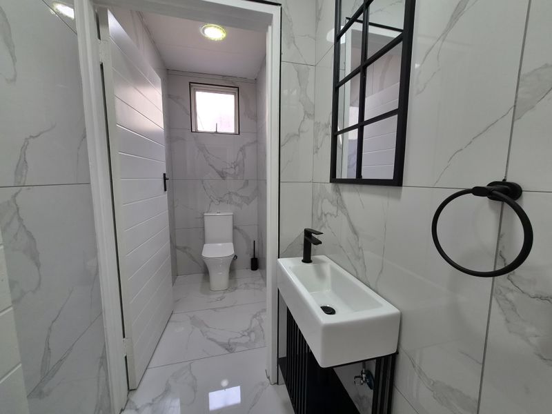 Modern guest bathroom featuring marble-look porcelain tiling, a sleek wall-mounted basin with black fixtures, and a contemporary black-framed mirror.