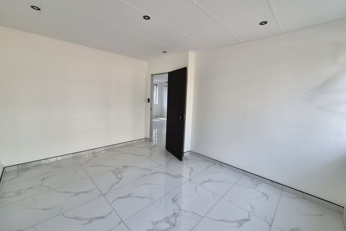 A bright, empty bedroom featuring modern marble-look floor tiles, recessed downlights, and a clean, neutral finish throughout.
