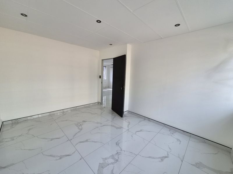 A bright, empty bedroom featuring modern marble-look floor tiles, recessed downlights, and a clean, neutral finish throughout.