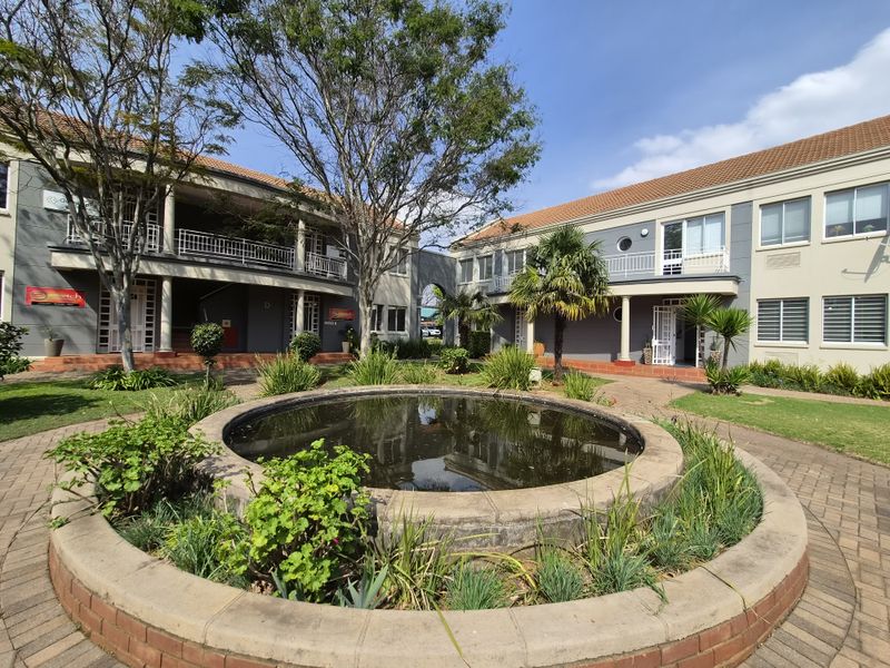 A well-maintained commercial courtyard featuring a central brick fountain, paved walkways, and multi-level office building facades with balconies.