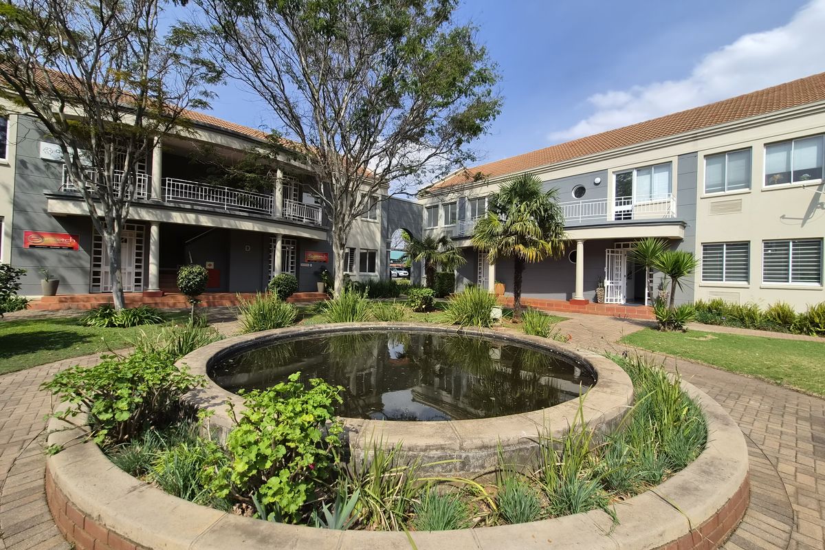 A well-maintained commercial courtyard featuring a central brick fountain, paved walkways, and multi-level office building facades with balconies.