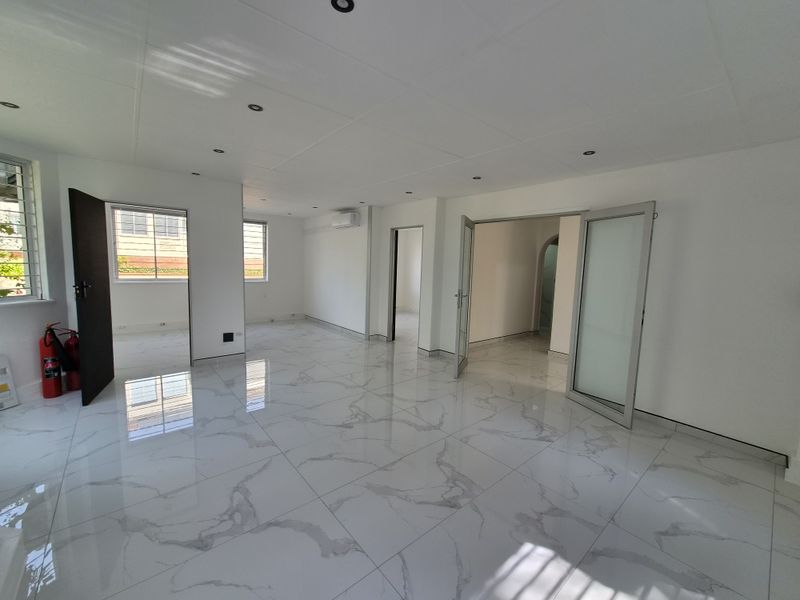 A bright, open-plan interior space featuring polished marble-look porcelain floor tiles, recessed lighting, and modern aluminium door and window frames.