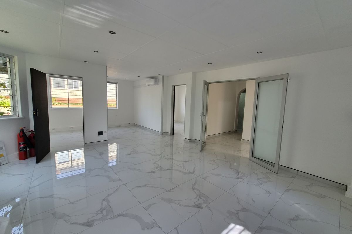 A bright, open-plan interior space featuring polished marble-look porcelain floor tiles, recessed lighting, and modern aluminium door and window frames.