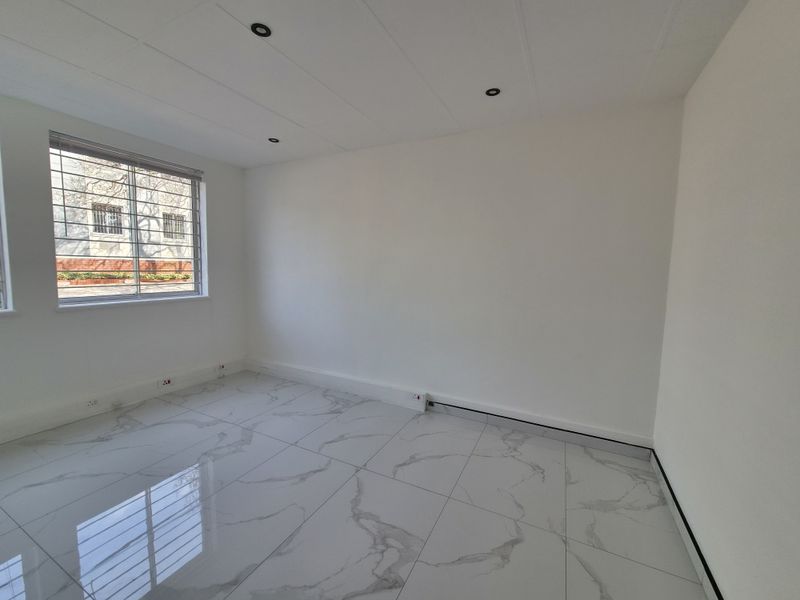 A bright, empty office space featuring modern marble-look porcelain floor tiles, recessed downlights, and a window fitted with security bars.
